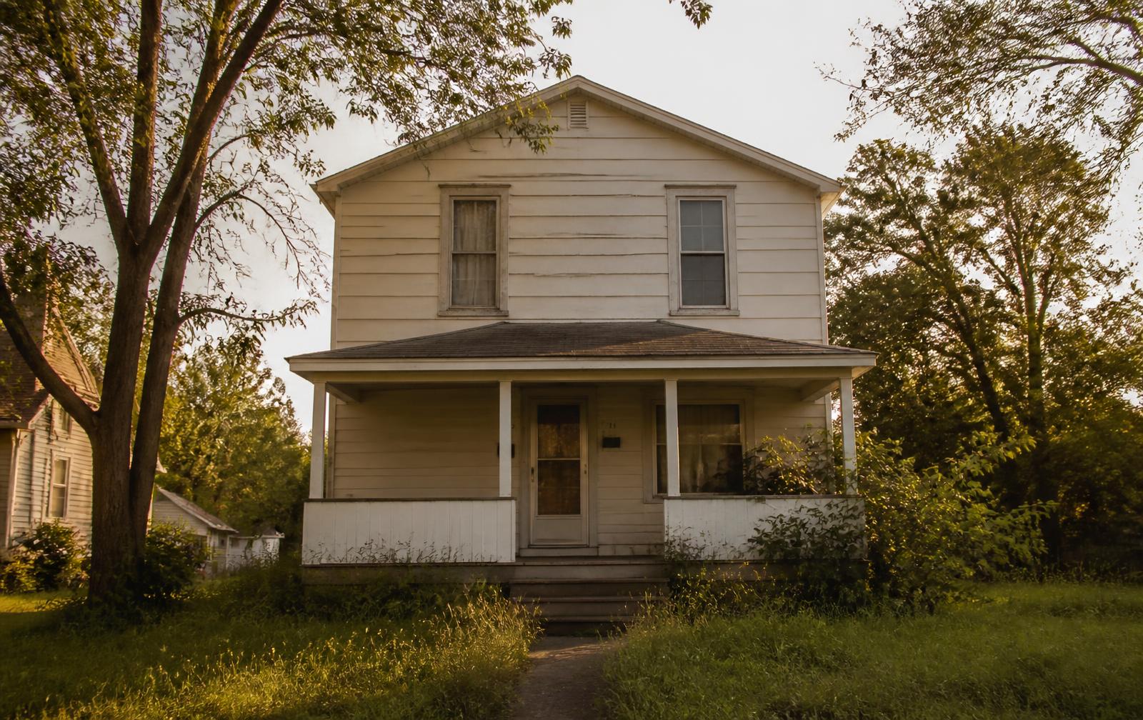 Two-storey house at golden hour with peeling paint and an overgrown yard
