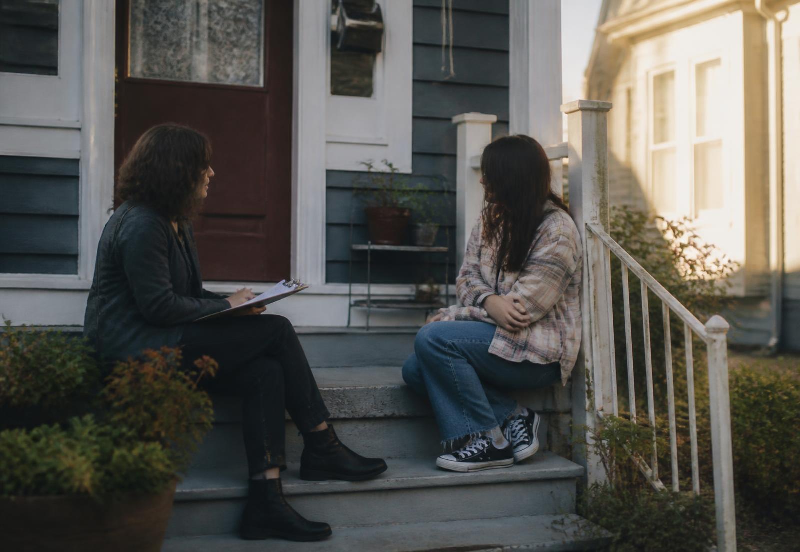 Two people talking on the front steps of an older house